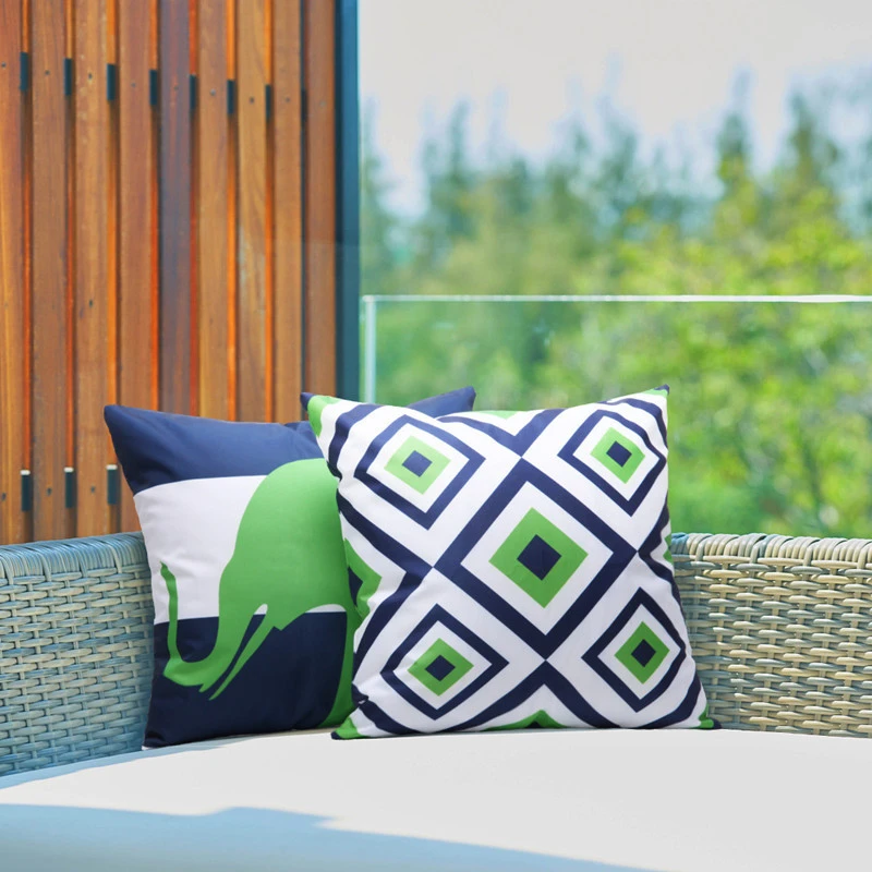 Navy green and white diamond throw pillow in front of other cushions on a wicker sofa